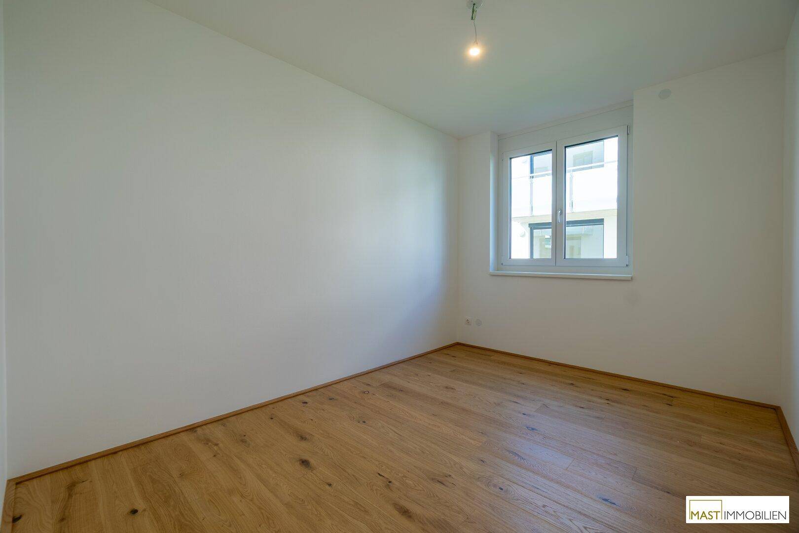 Leeres Schlafzimmer mit hellem Holzfußboden und einem Fenster mit Blick nach draußen.