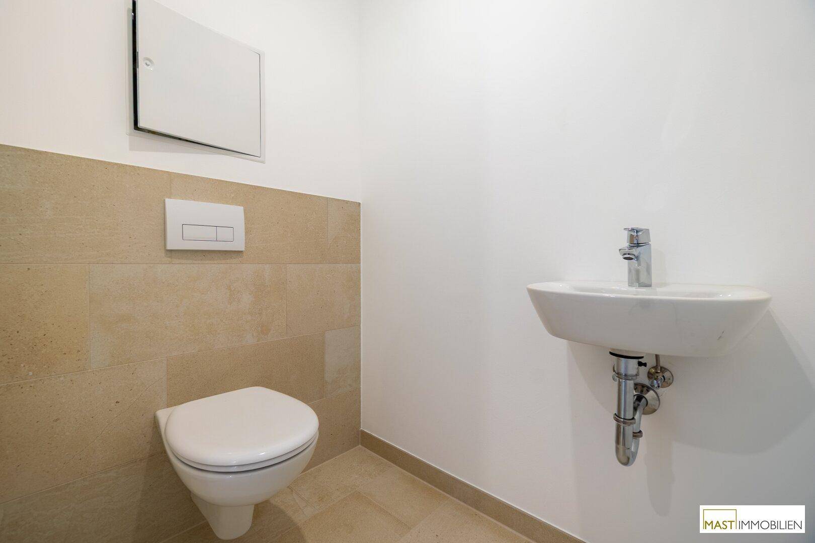 Separates Gäste-WC mit wandhängender Toilette, kleinem Waschbecken und beigen Fliesen.