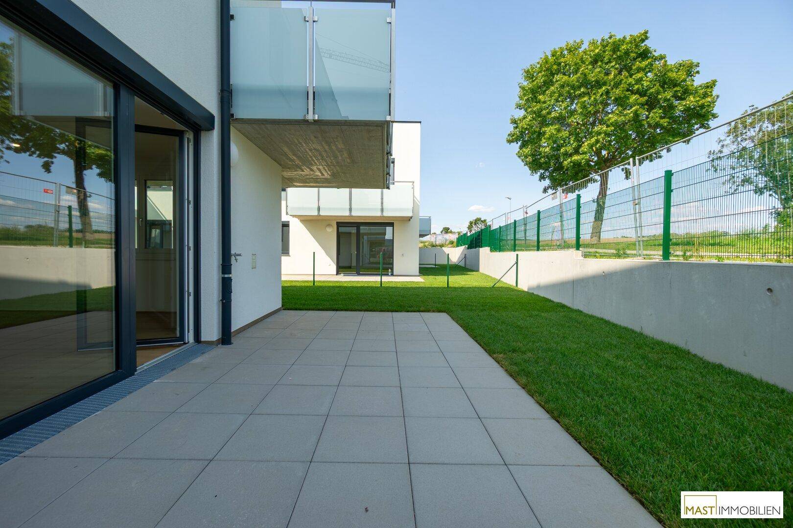 Gepflasterte Terrasse mit Zugang zum Garten und Blick auf einen großen Baum.