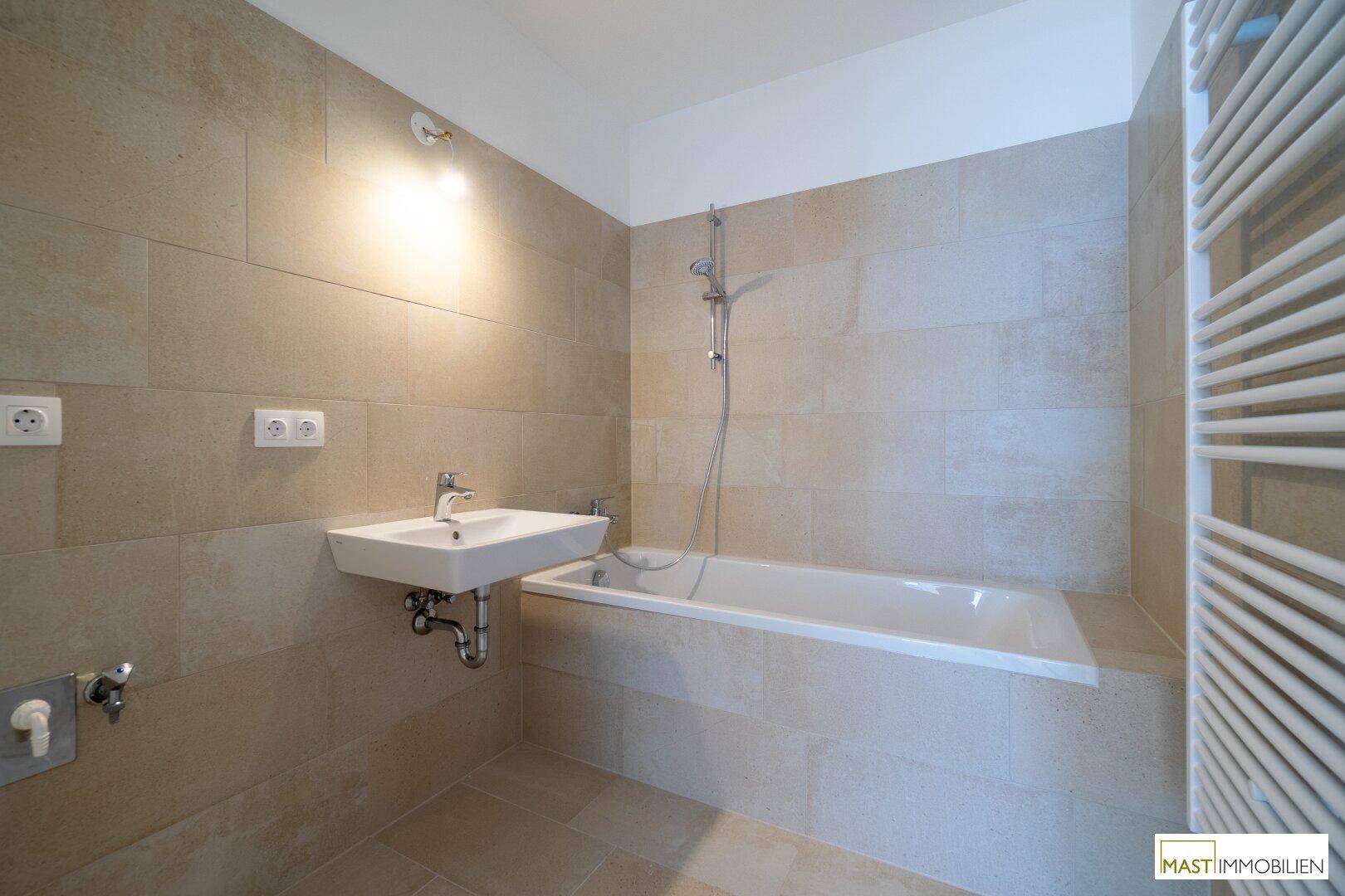 Modernes Badezimmer mit beigefarbenen Fliesen, Badewanne mit Duschfunktion und beheiztem Handtuchhalter.