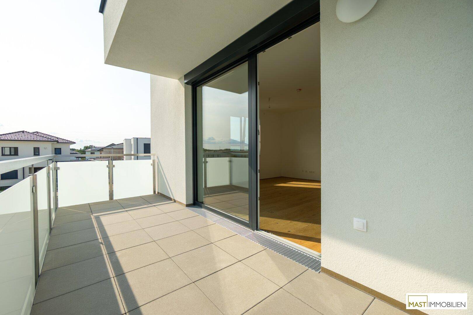 Sonniger Balkon mit Fliesenboden und großer Glasschiebetür, die in einen hellen Innenraum führt.