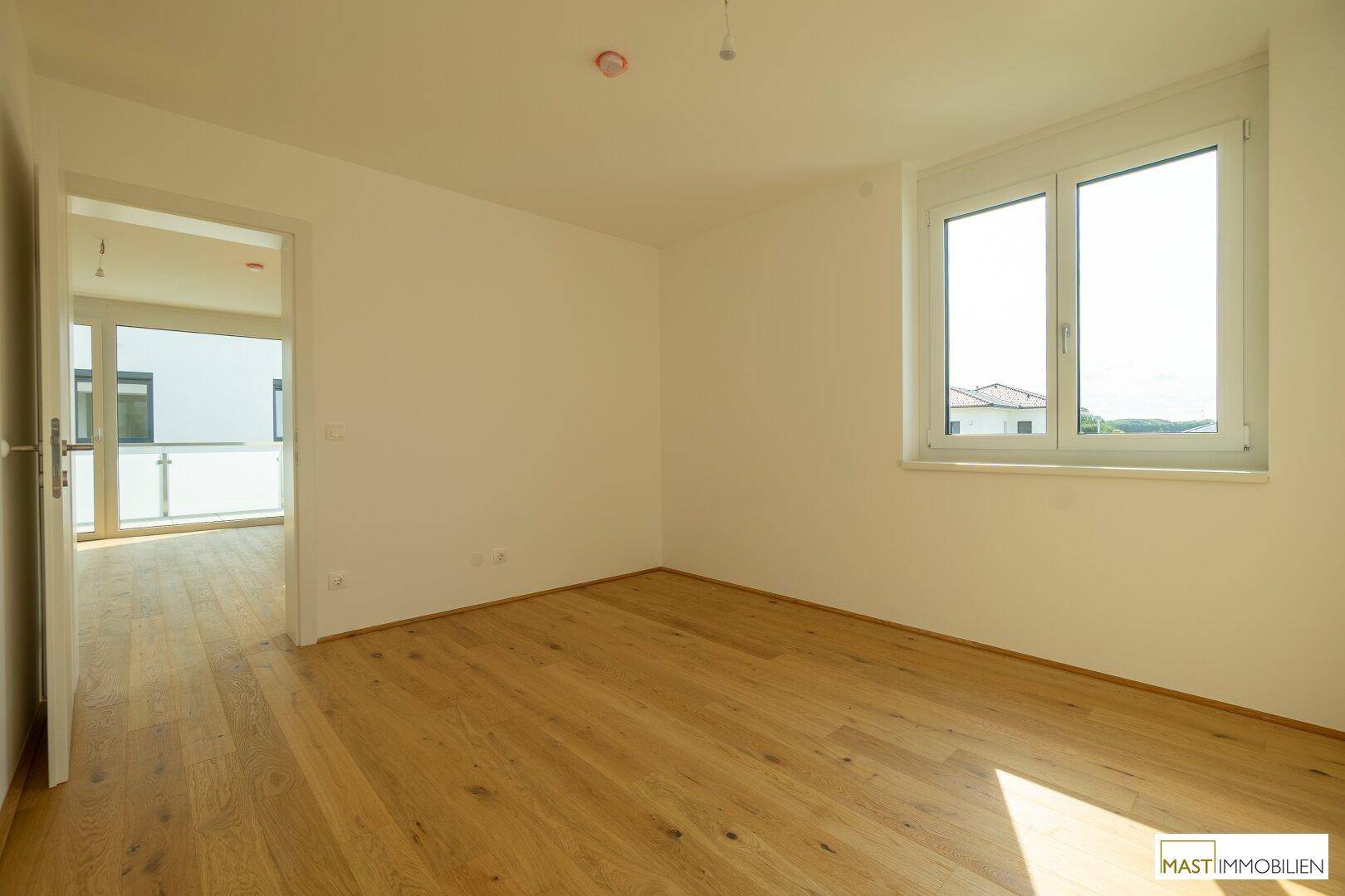 Lichtdurchflutetes Schlafzimmer mit hellem Eichenparkett und Zugang zu einem weiteren Raum mit Balkon.
