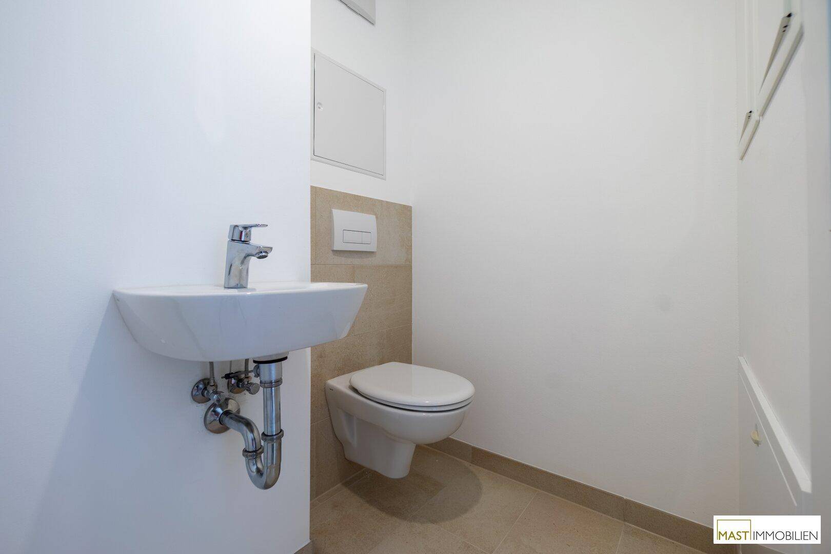 Funktionale Gästetoilette mit wandhängendem WC und kleinem Waschbecken, in neutralen Farbtönen gehalten.