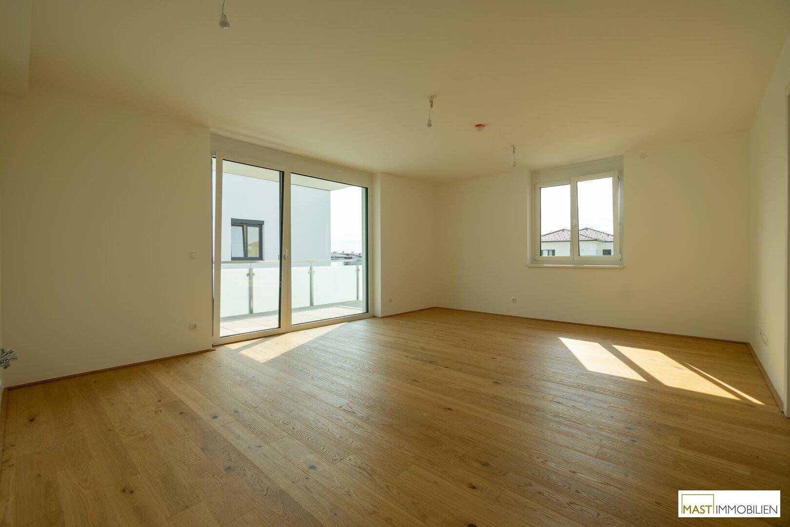 Geräumiger, heller Raum mit Eichenparkett und Zugang zu einem Balkon durch eine große Glasschiebetür.