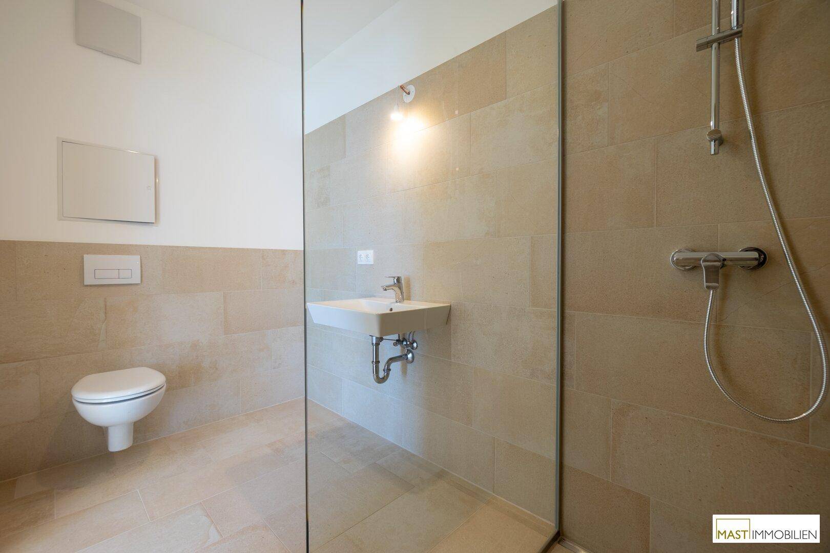 Modernes Badezimmer mit beigefarbenen Fliesen, wandhängendem WC und einer geräumigen begehbaren Dusche.