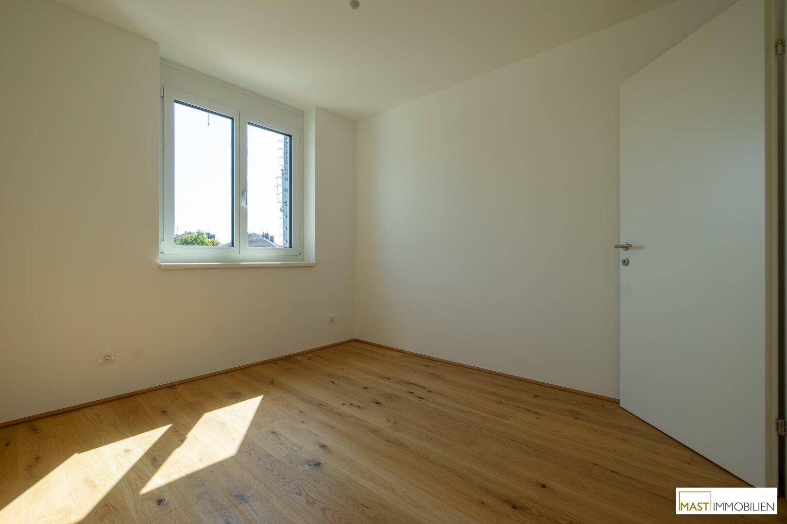 Freundliches Zimmer mit hellem Holzboden und Fenster, ideal als Schlaf- oder Arbeitszimmer.