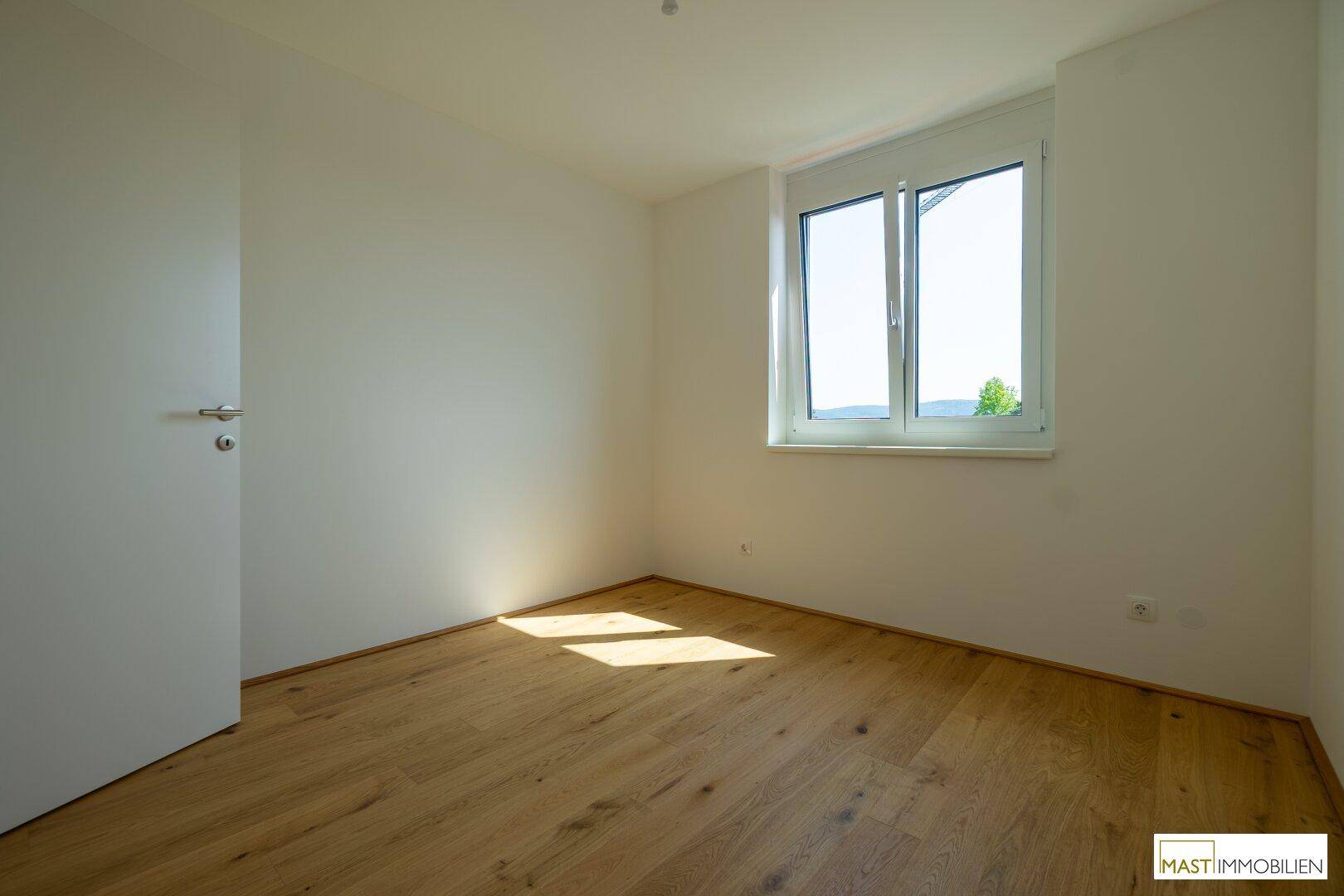 Helles Schlafzimmer mit Holzboden und einem großen Fenster, das einen weiten Blick bietet.