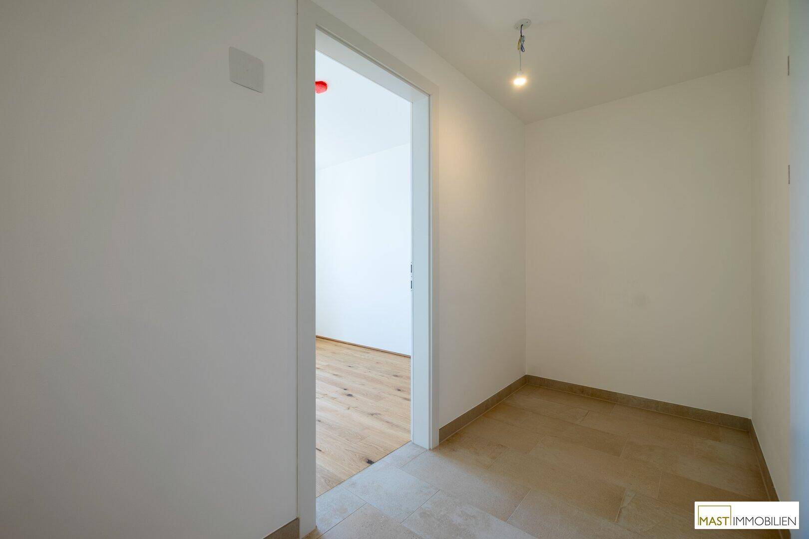 Heller Eingangsbereich mit Fliesenboden, der zu einem Zimmer mit Holzboden führt.