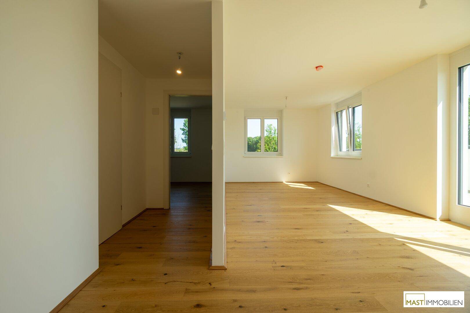 Geräumiger, heller Raum mit Holzboden und offenem Zugang zu einem weiteren Bereich der Wohnung.