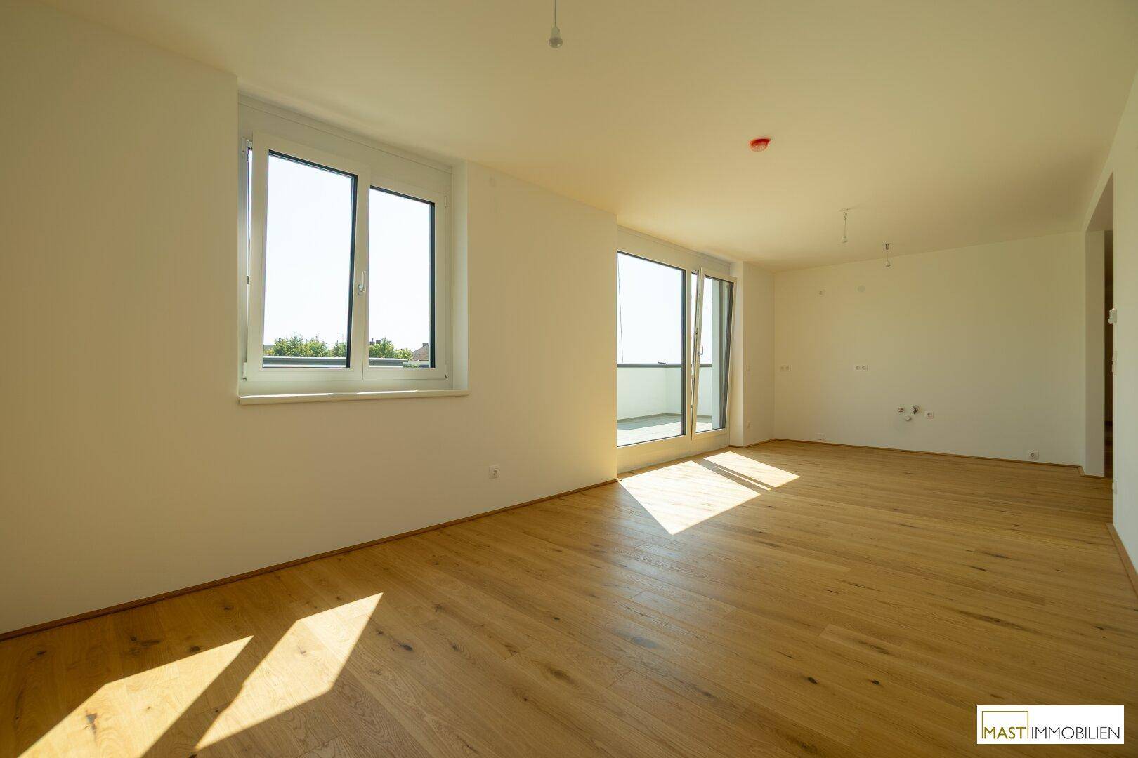 Lichtdurchfluteter Wohnraum mit hellem Holzboden und großen Fenstern, die auf die Terrasse führen.