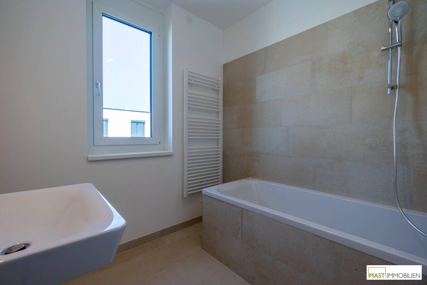 Modernes Badezimmer mit Badewanne, Wandwaschbecken, beheiztem Handtuchhalter und Fenster.