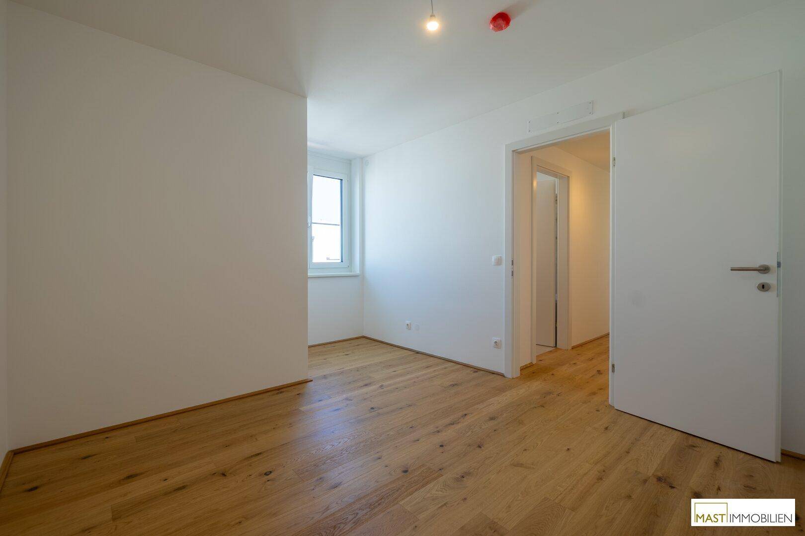 Lichtdurchflutetes Zimmer mit Holzboden und weißer Wandgestaltung, ideal als Schlaf- oder Arbeitszimmer.
