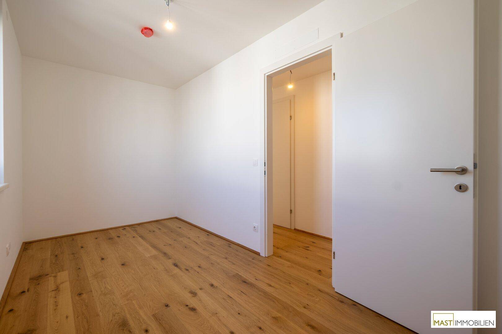 Helles, leeres Zimmer mit warmem Holzboden und weiß gestrichenen Wänden, bereit zur Einrichtung.