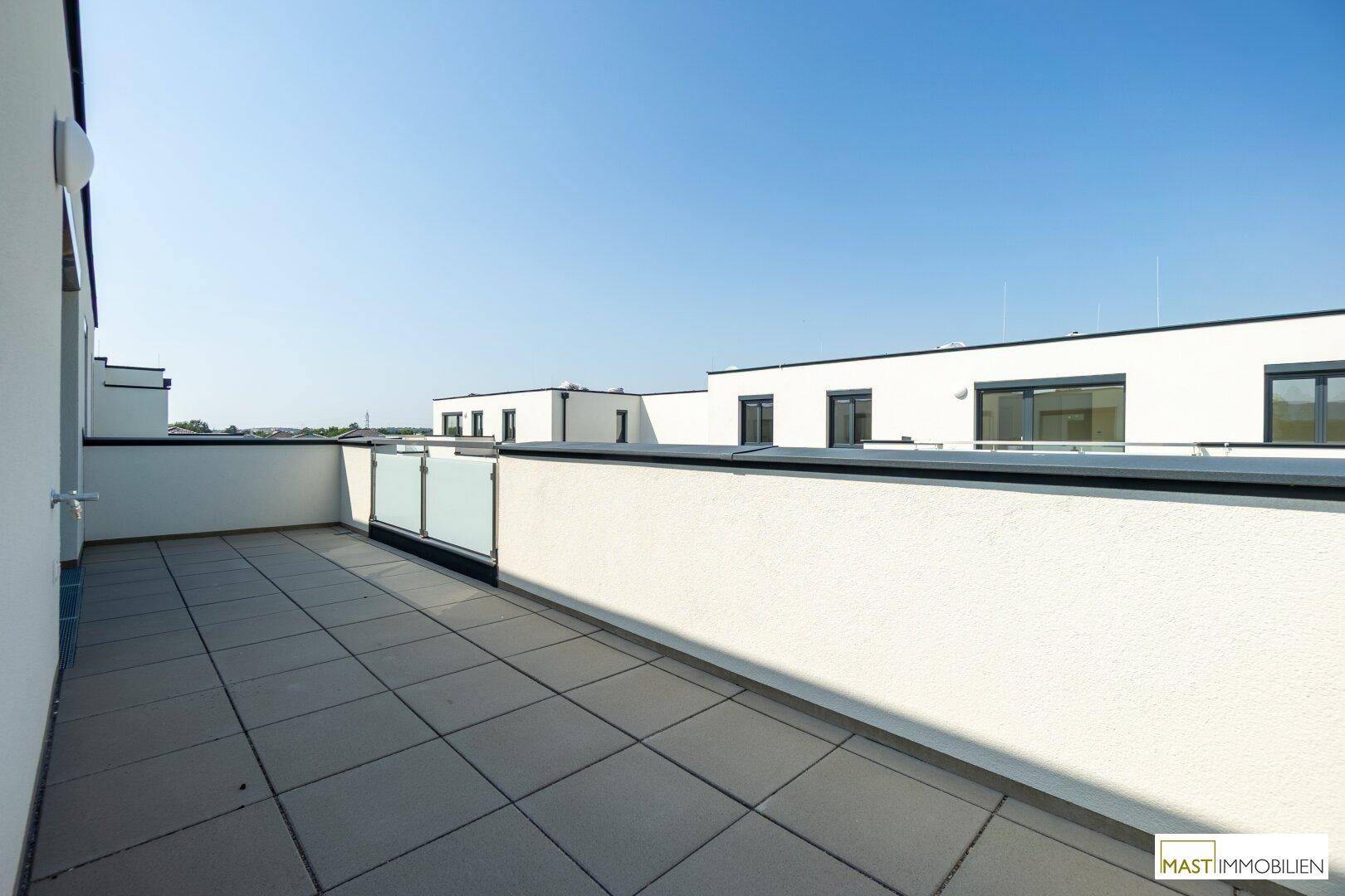 Sonnige Terrasse mit Fliesenboden und Blick auf die moderne Architektur der Wohnanlage.