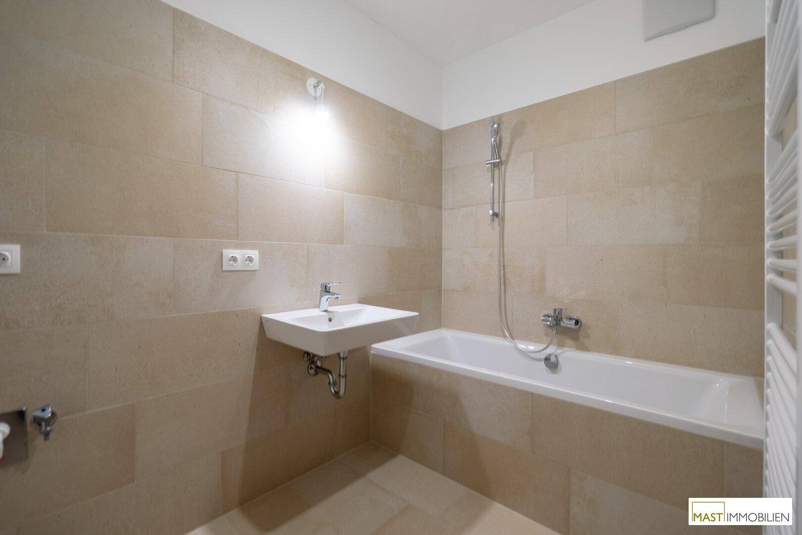 Modernes Badezimmer mit Badewanne, Waschbecken und beigefarbenen Fliesen, in neuwertigem Zustand.