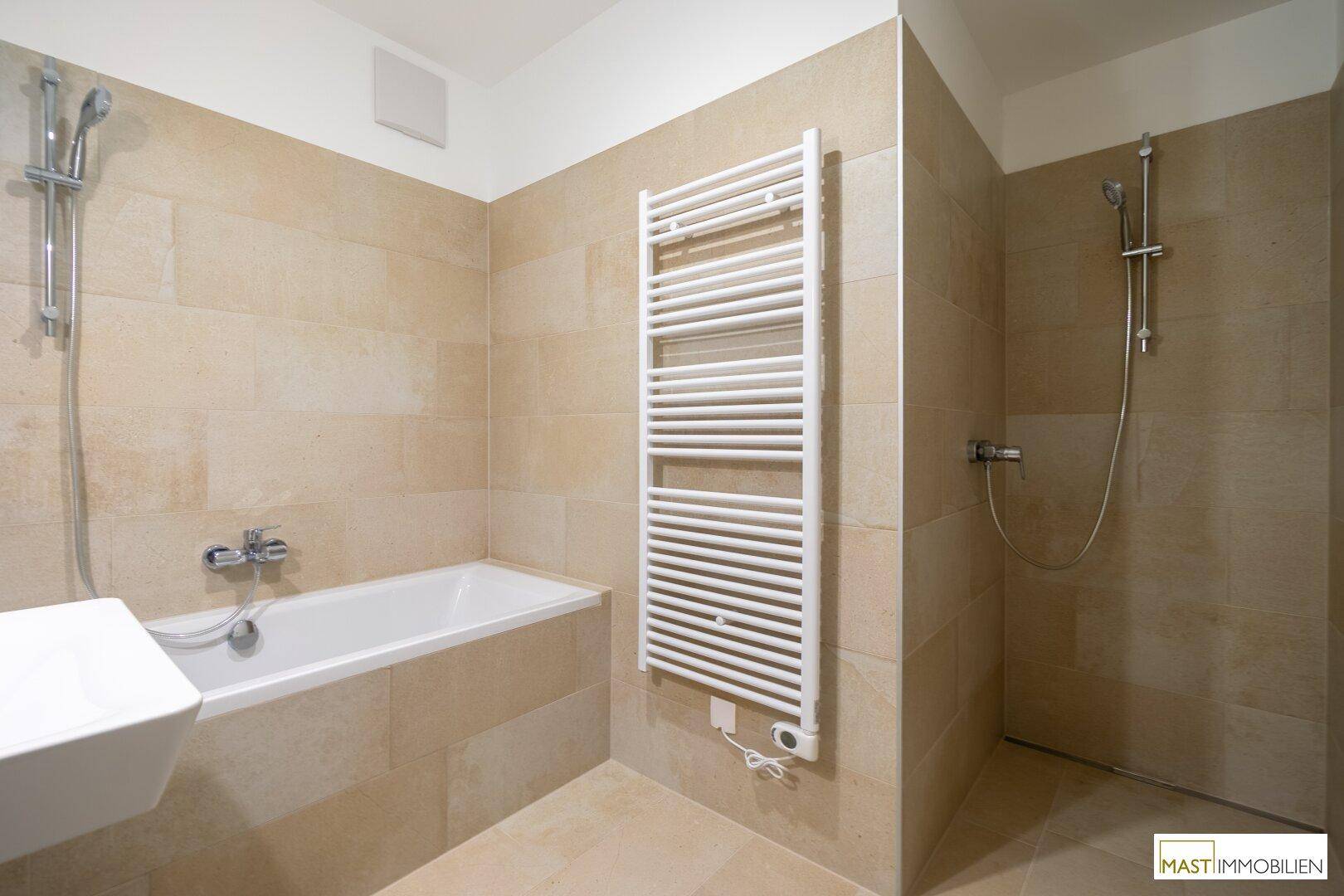 Badezimmer mit Badewanne, separater Dusche und beheiztem Handtuchhalter, komplett gefliest.