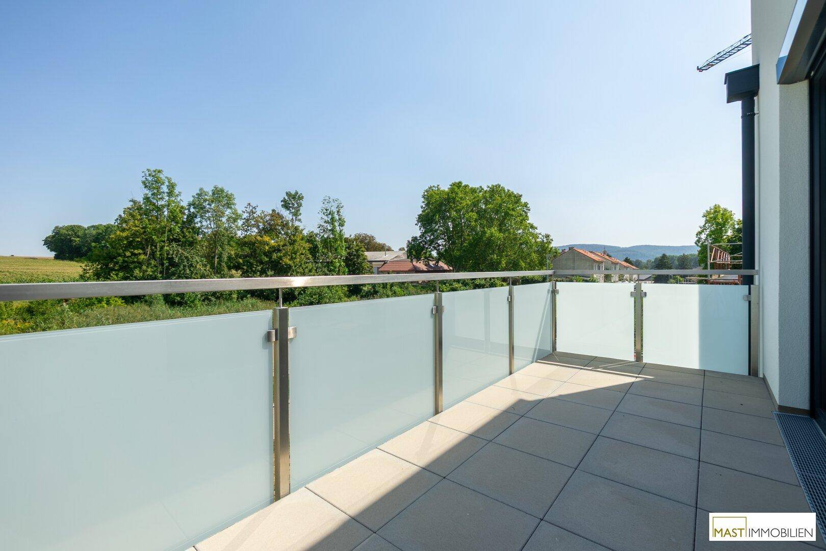 Sonniger Balkon mit Fliesenboden und moderner Glasbrüstung, bietet einen weiten Blick ins Grüne.