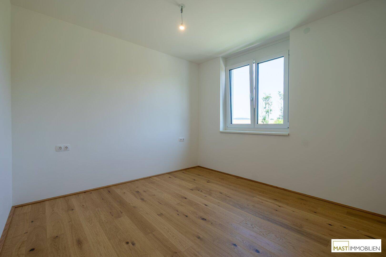 Ruhiges Schlafzimmer mit hellem Holzboden und einem Fenster, das viel Tageslicht hereinlässt.