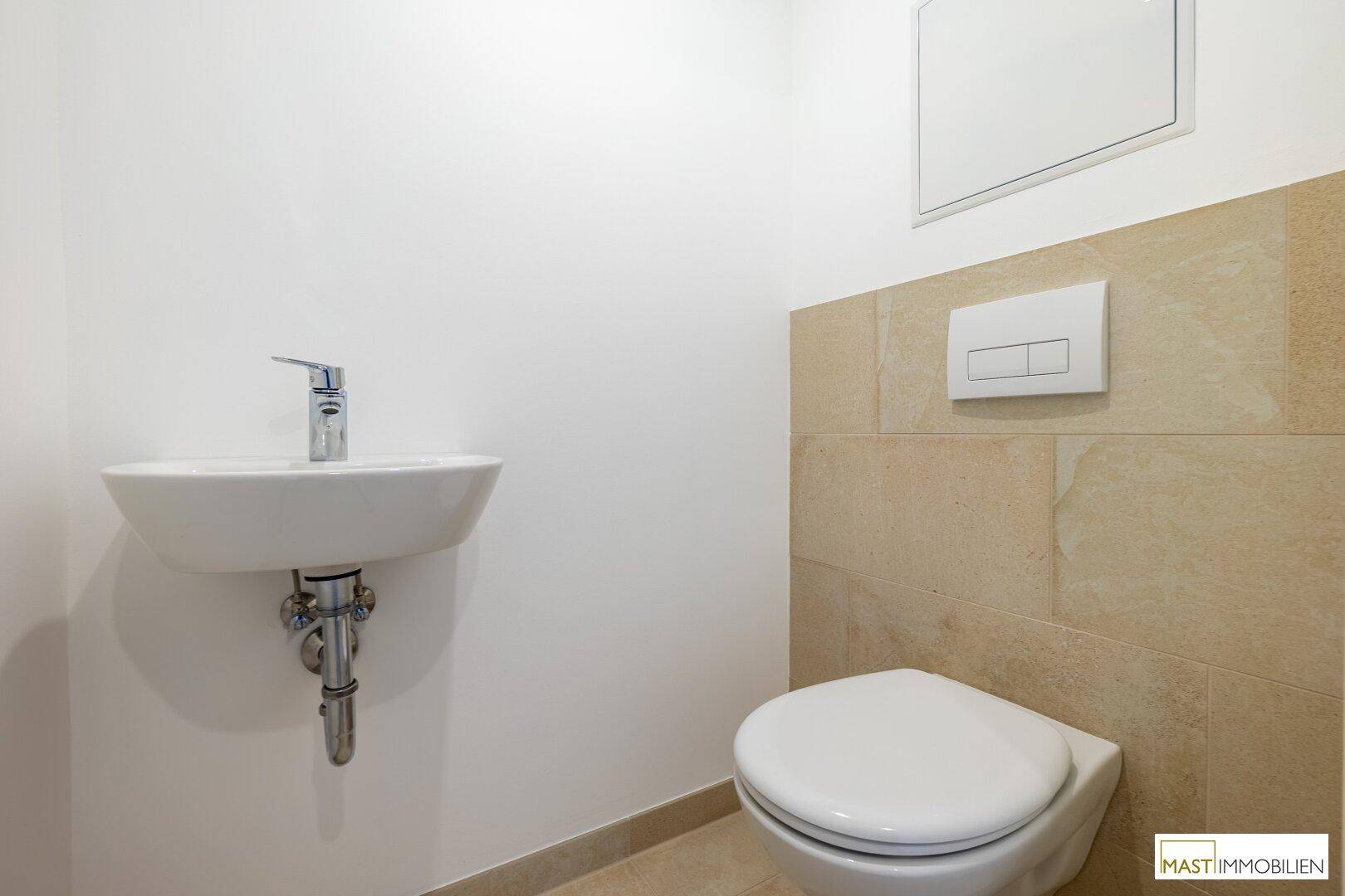 Gäste-WC mit wandhängender Toilette und kleinem Waschbecken, teilweise gefliest.