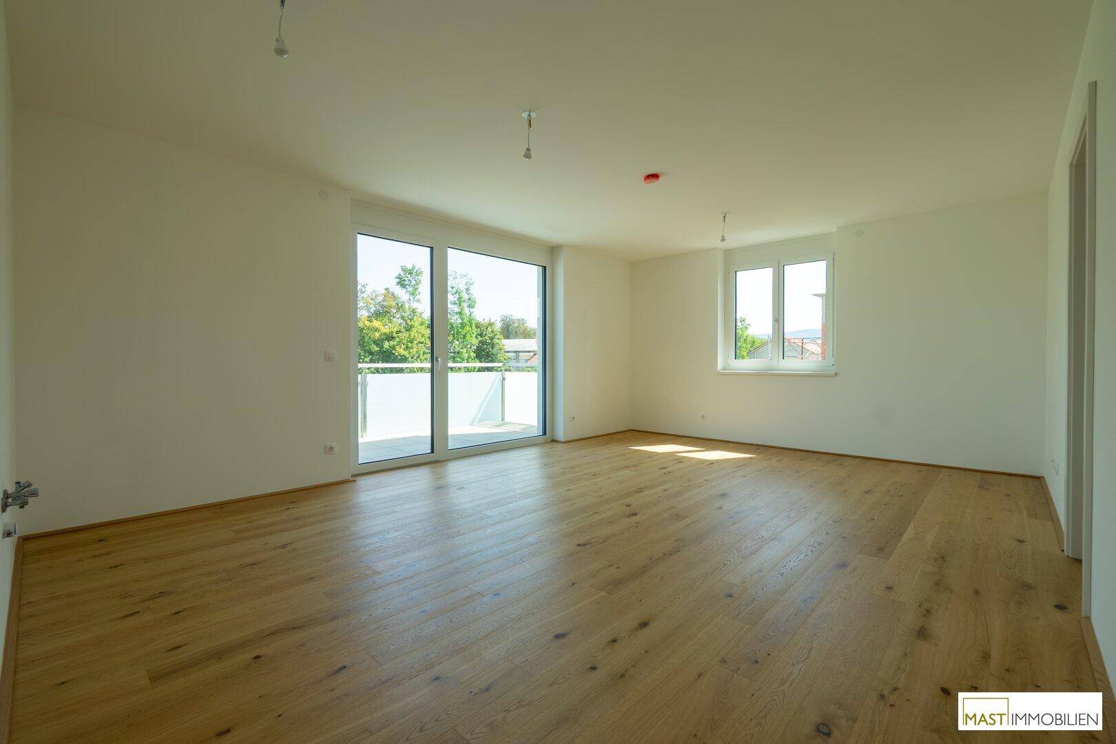 Geräumiges, helles Zimmer mit Holzdielenboden und Zugang zu einem Balkon oder einer Terrasse.