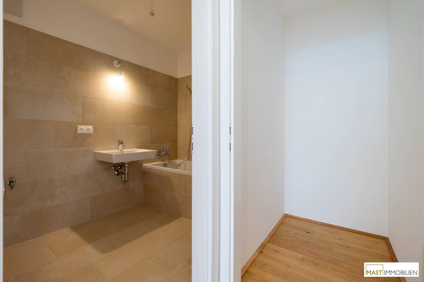 Modernes Badezimmer mit beigefarbenen Fliesen, Waschbecken und Badewanne, teilweise sichtbar.