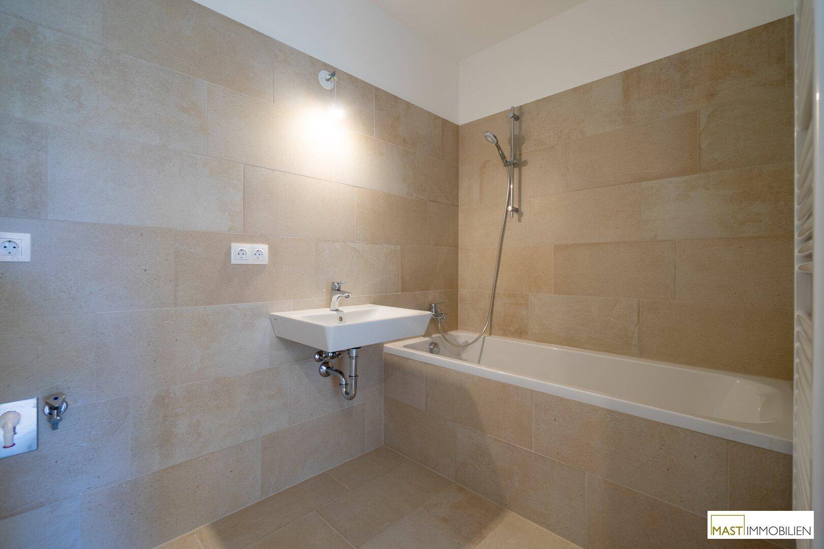 Modernes Badezimmer mit beigefarbenen Wand- und Bodenfliesen, ausgestattet mit Badewanne und Waschbecken.