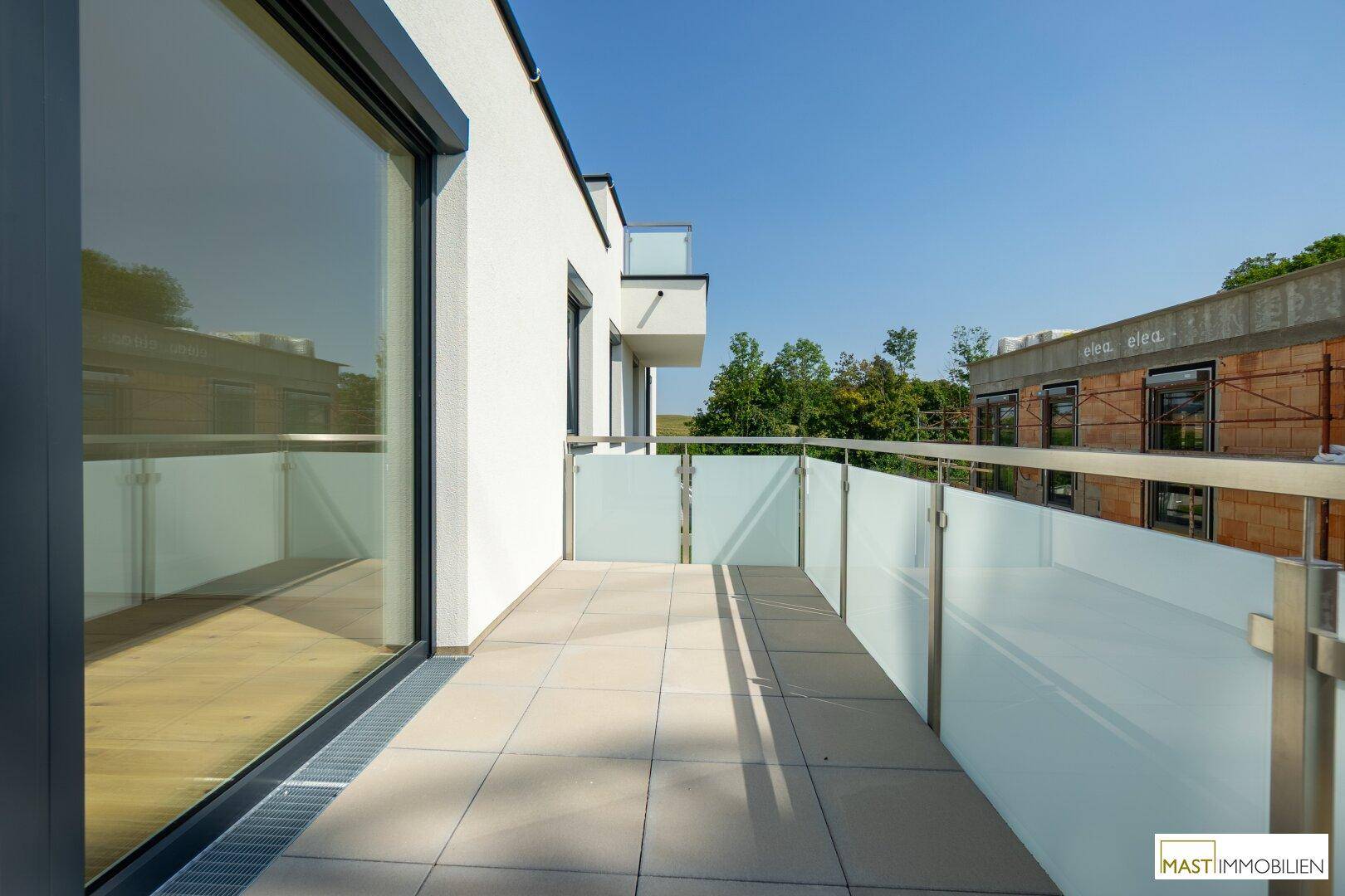 Moderner Balkon mit Fliesenboden und Milchglasgeländer, bietet einen weiten Blick in die Umgebung.