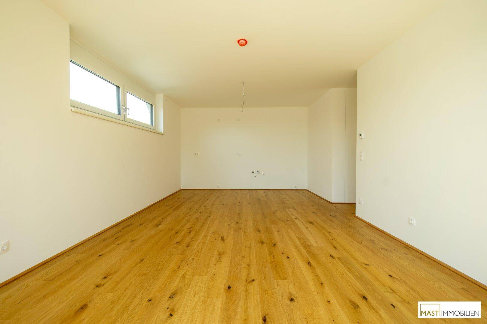 Helles, leeres Zimmer mit Holzparkett und Fenster, bietet viel Tageslicht für verschiedene Nutzungen.