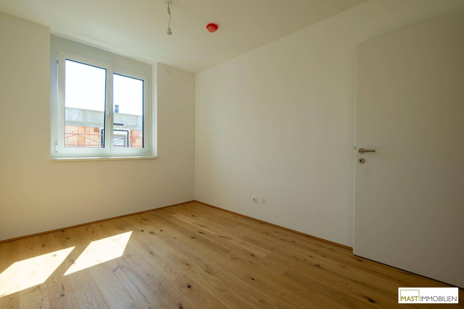 Helles Schlafzimmer mit Holzboden und Fenster, das eine angenehme Atmosphäre für Ruhe schafft.