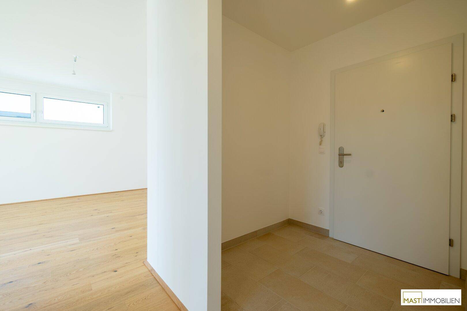 Eingangsbereich mit Fliesenboden und weißer Tür, führt zu einem hellen Zimmer mit Holzparkett.