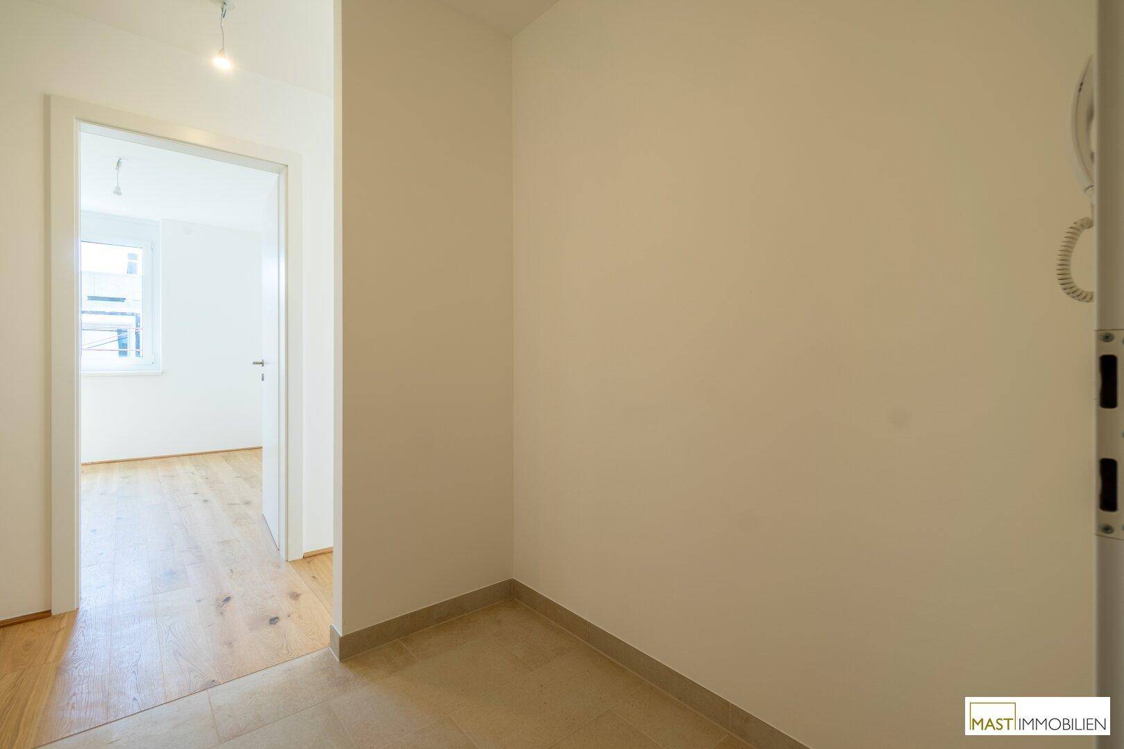 Heller Flur mit Fliesenboden, der den Übergang zu einem Zimmer mit Holzparkett markiert.