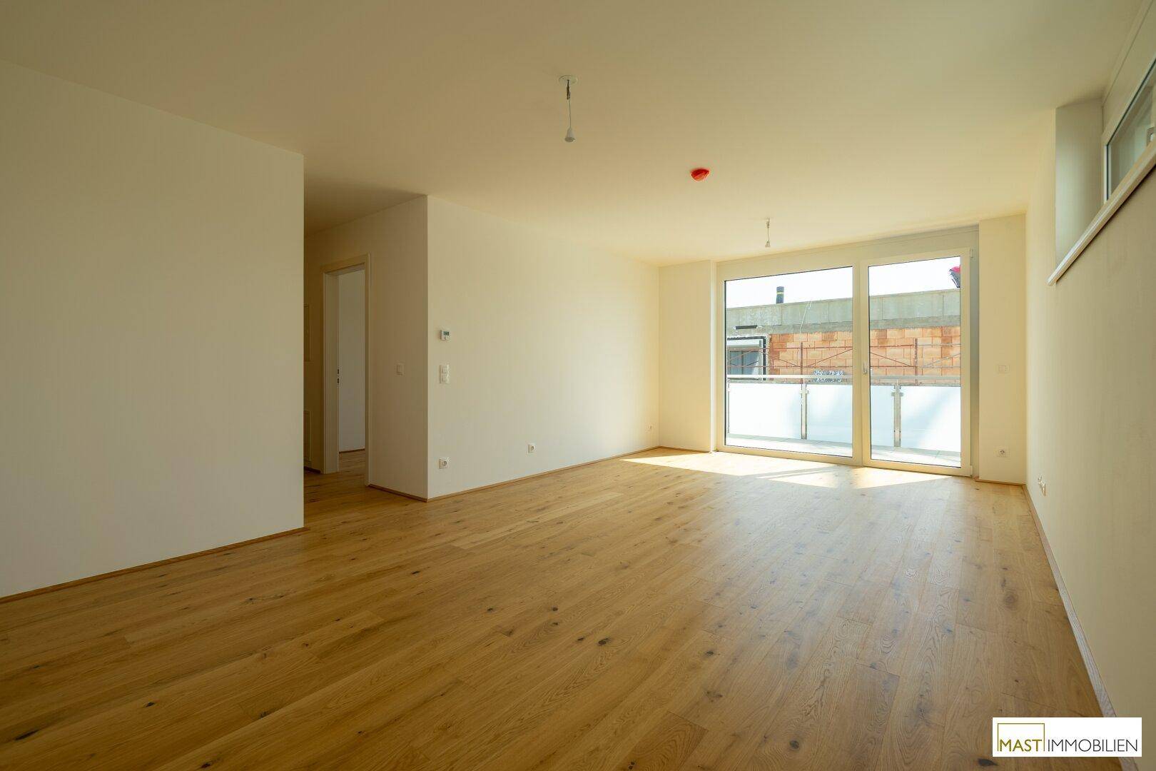 Geräumiges, leeres Wohnzimmer mit hellem Holzparkett und großen Fenstern, bereit zur individuellen Gestaltung.