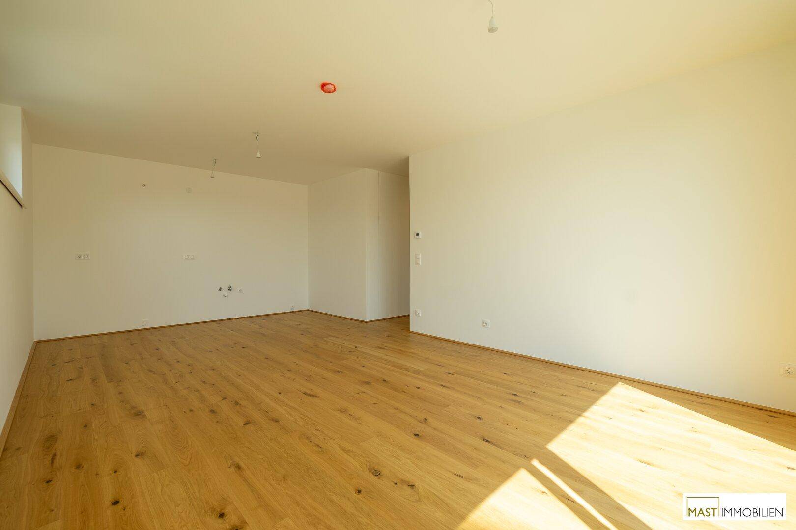 Lichtdurchfluteter, leerer Raum mit Eichenparkett und weißen Wänden, ideal für ein Wohnzimmer.