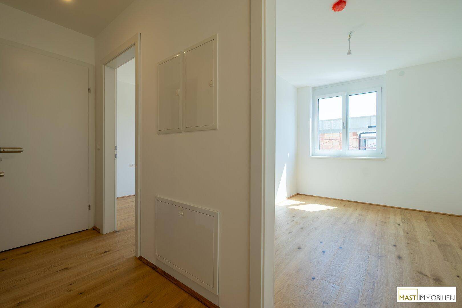Heller Flur mit Holzparkett, der zu einem weiteren Zimmer mit Fenster und Tageslicht führt.