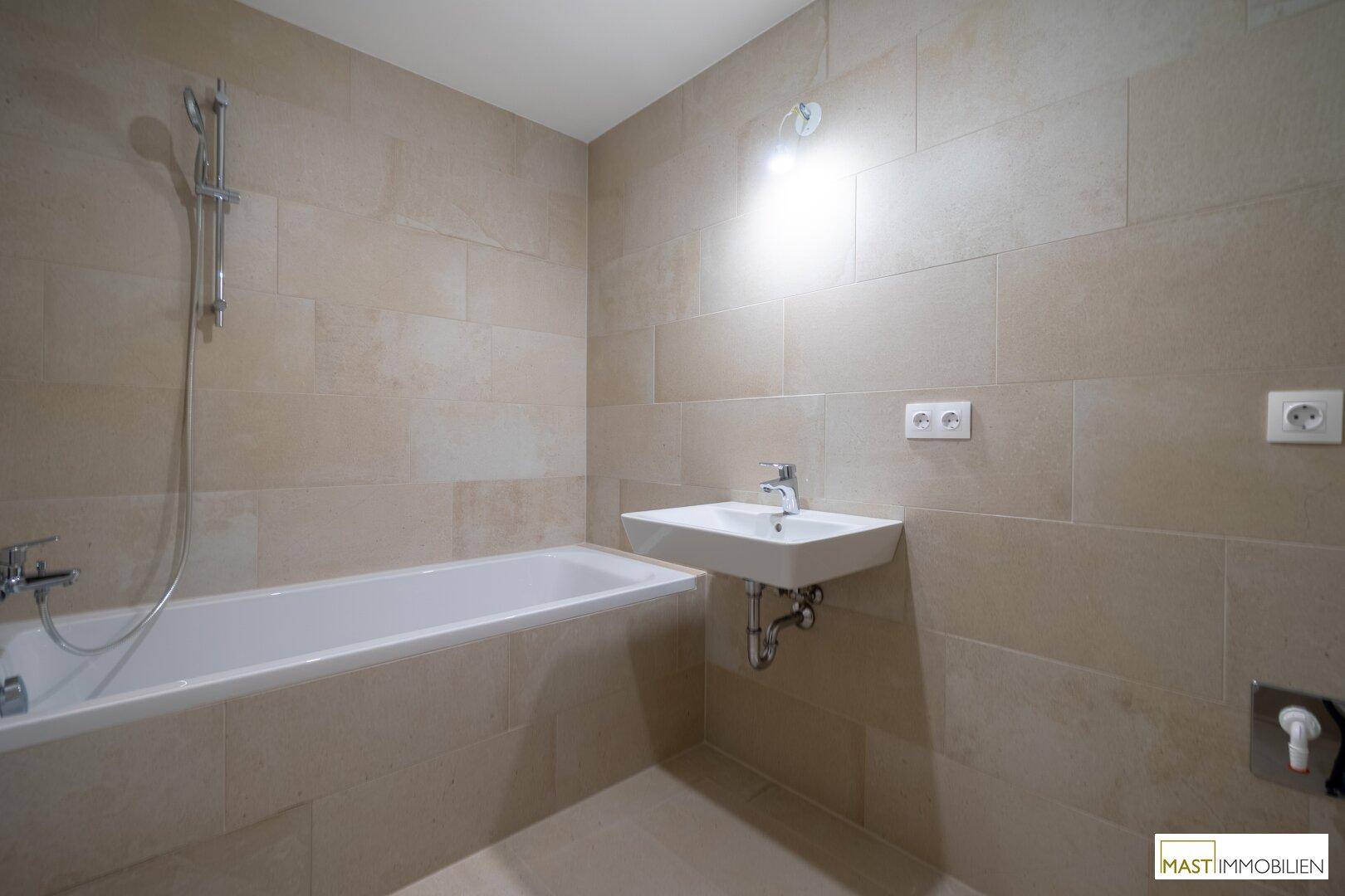 Zeitgemäßes Badezimmer mit Badewanne, Waschbecken und eleganten beigefarbenen Wandfliesen.