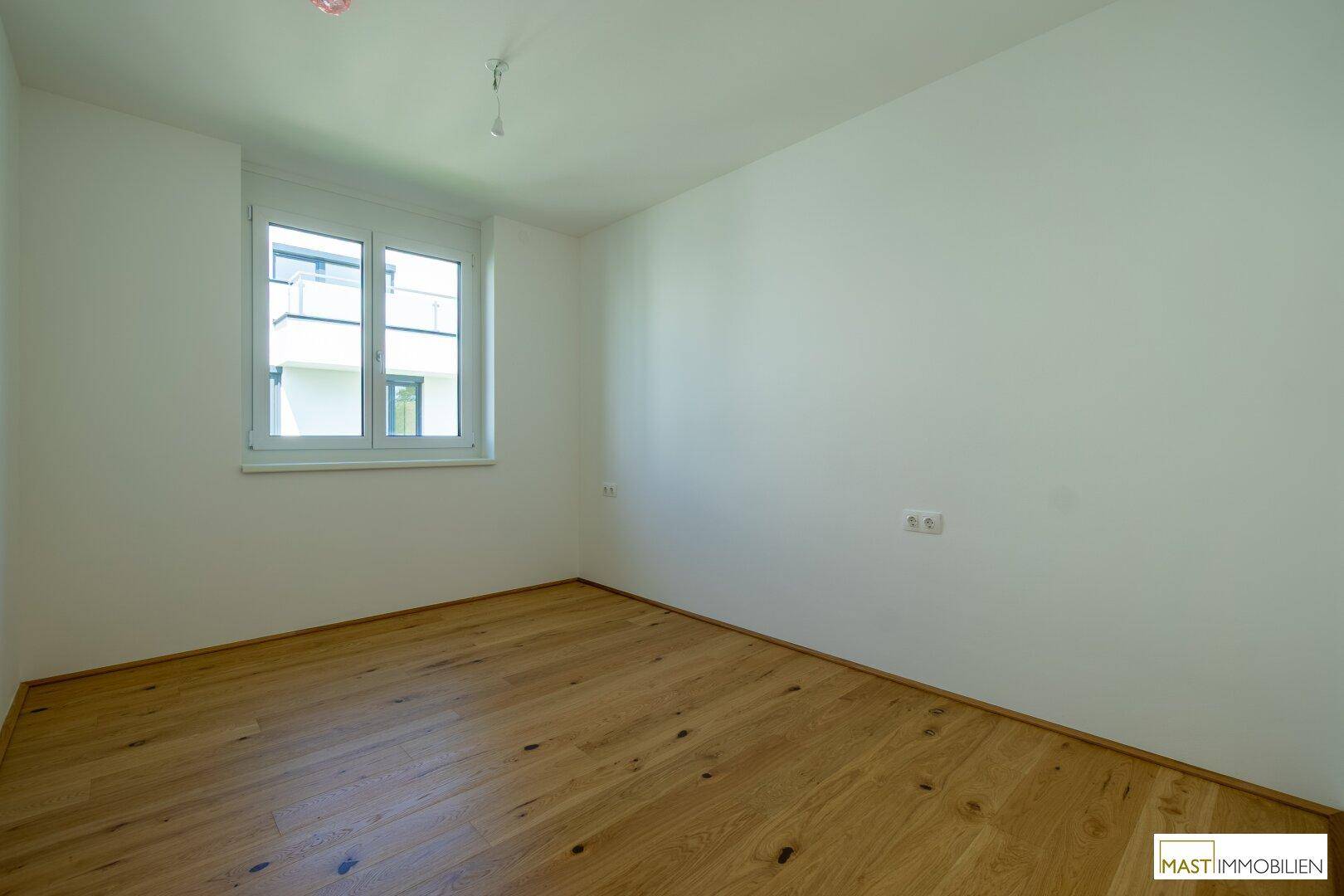 Helles Zimmer mit Eichenparkett und weiß gestrichenen Wänden, bereit zur individuellen Gestaltung.
