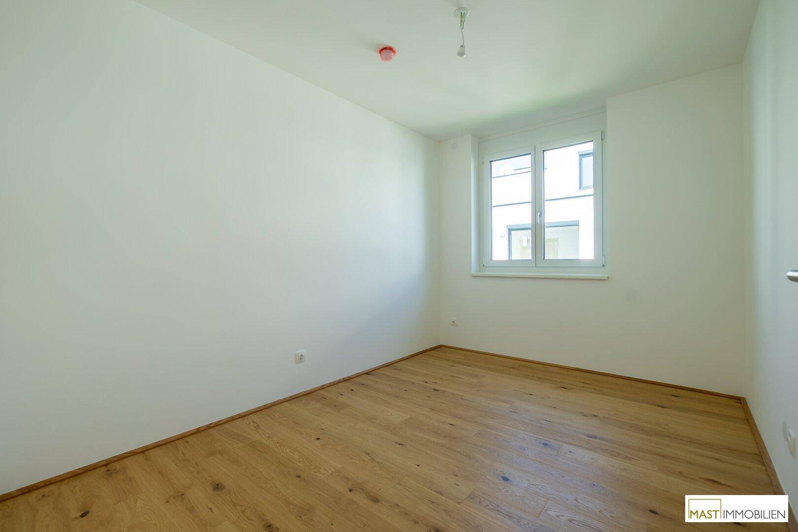 Ruhiges Schlafzimmer mit hellem Parkettboden und großem Fenster, bietet viel Tageslicht.