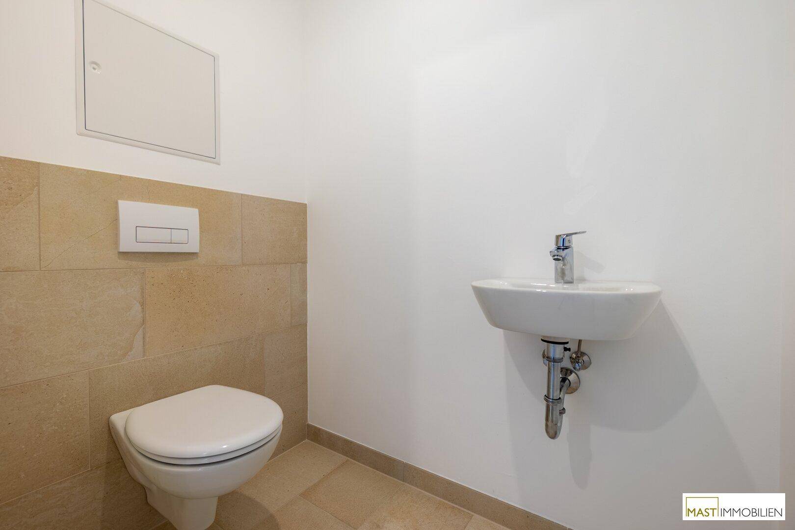 Separates Gäste-WC mit wandhängender Toilette und kleinem Handwaschbecken.