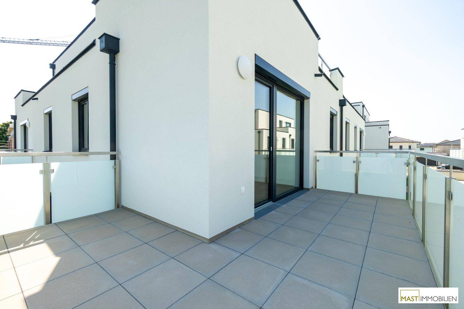 Geräumige Terrasse mit modernen Fliesen und Zugang zum Innenbereich des Neubaus.