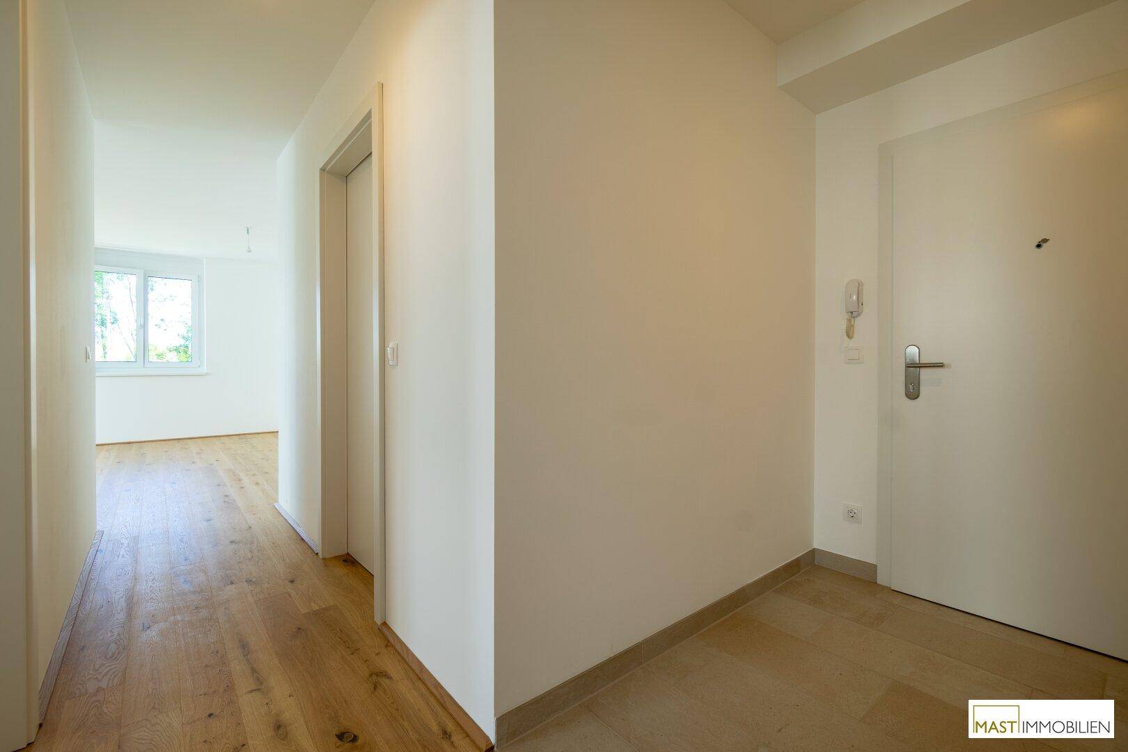 Heller Eingangsbereich mit Fliesenboden, der in einen Flur mit Holzparkett übergeht.