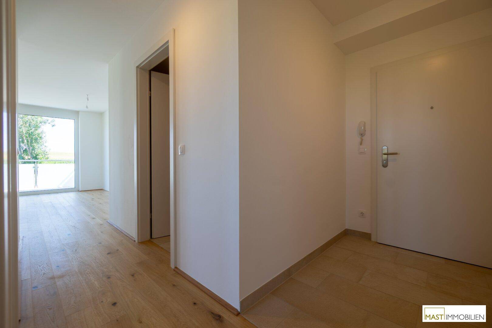 Heller Flur mit modernem Holzfußboden und weißen Wänden, der zu weiteren Räumen führt.