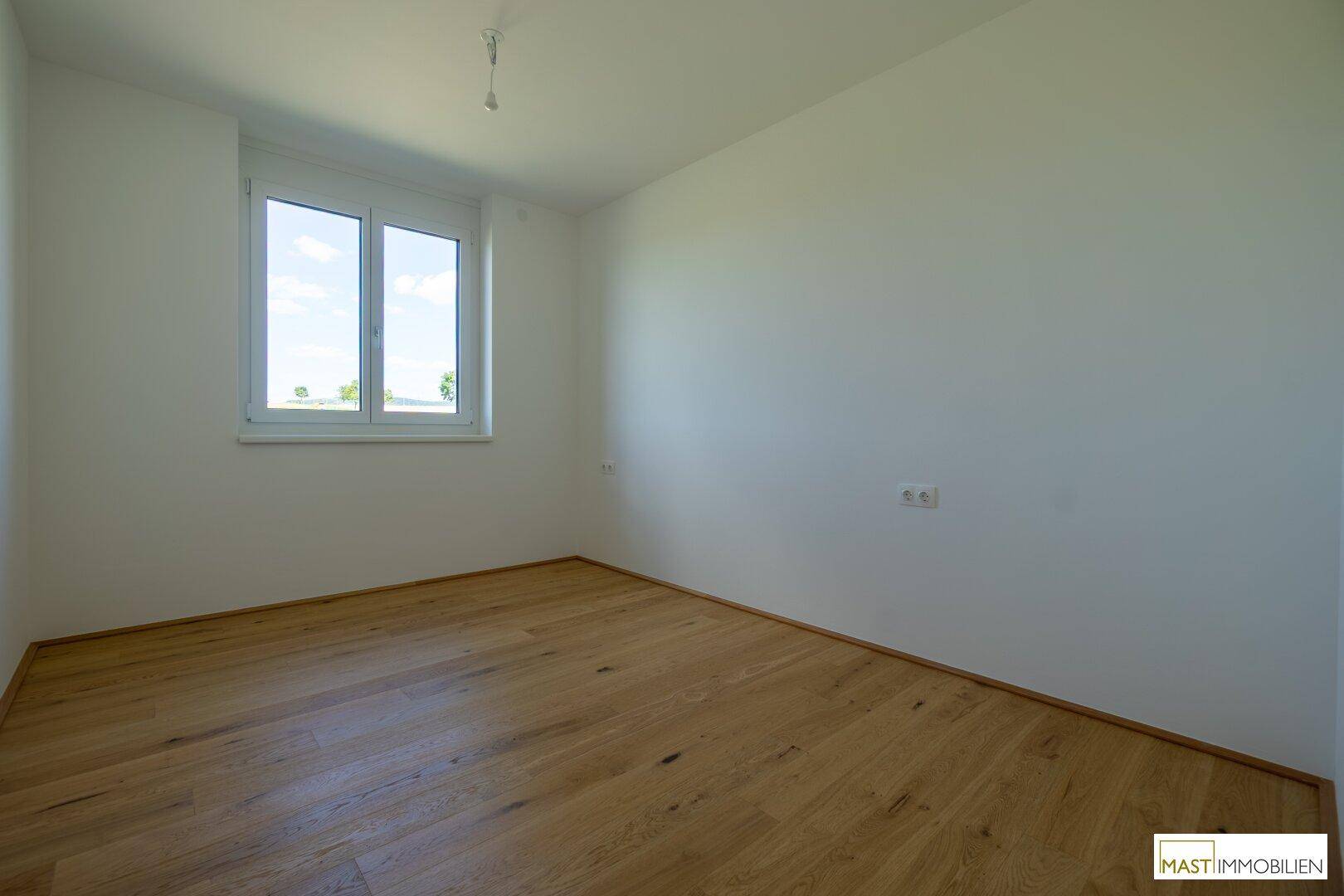Leeres Schlafzimmer mit hellem Holzparkett und einem Fenster, das viel Tageslicht bietet.