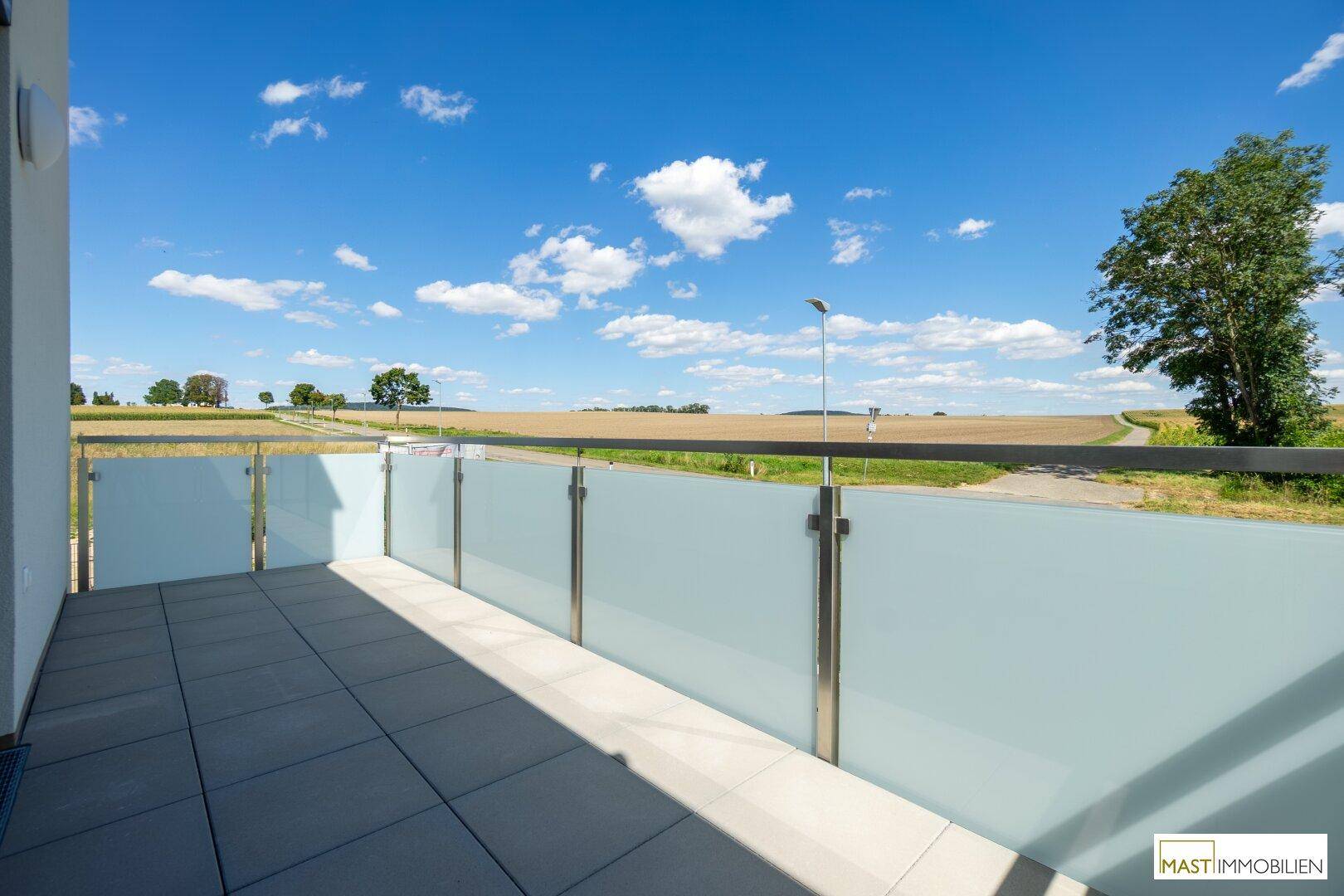 Sonniger Balkon mit modernem Glasgeländer und weitem Ausblick auf die grüne Landschaft.