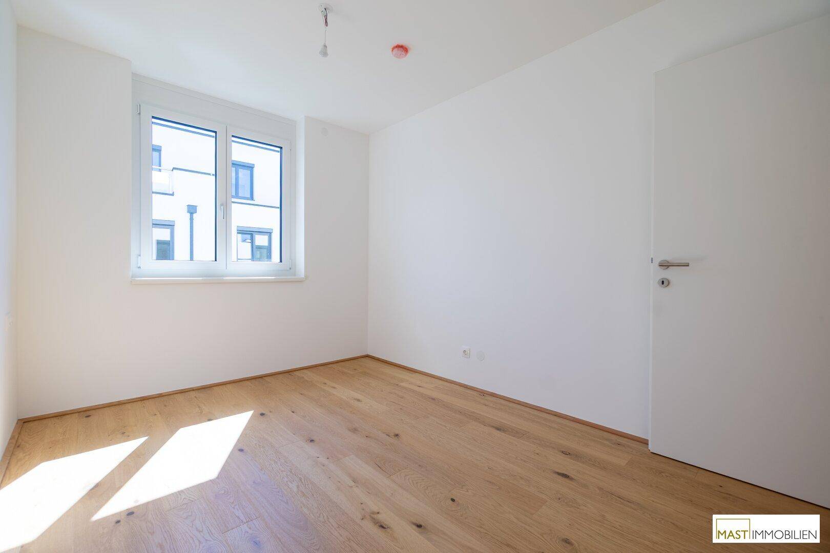 Freundliches Zimmer mit Parkettboden und großem Fenster für viel Tageslicht.