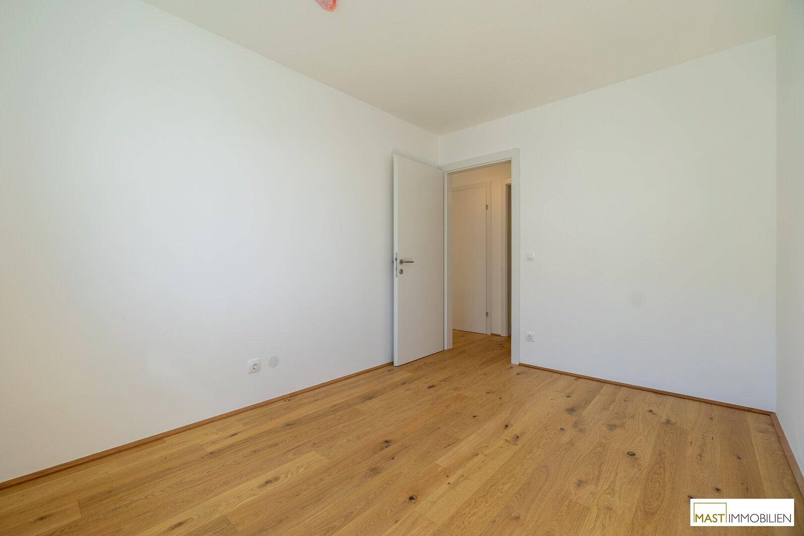 Geräumiges Zimmer mit Holzboden und Zugang zu weiteren Räumen, vielseitig nutzbar.