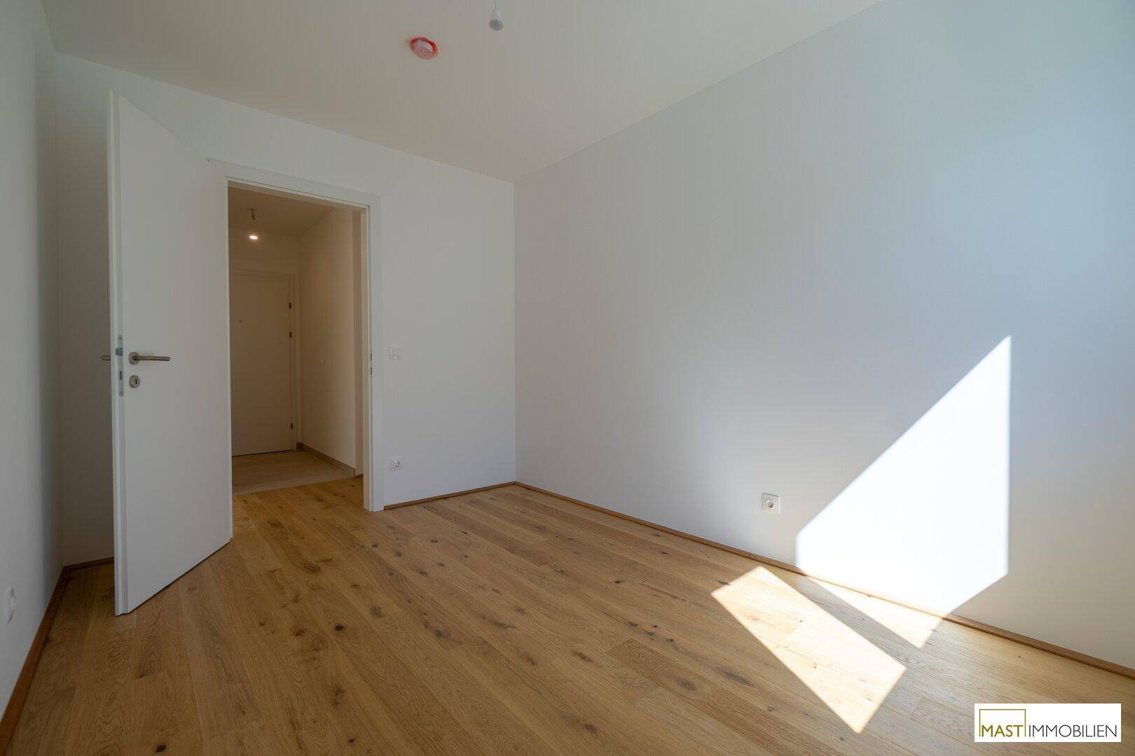 Ruhiges Schlafzimmer mit hellem Parkettboden und weiß gestrichenen Wänden.