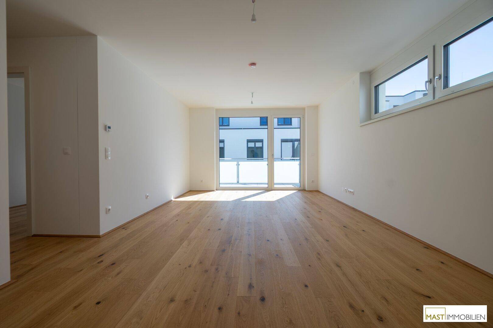 Lichtdurchfluteter Wohnbereich mit hochwertigem Parkettboden und Zugang zum Balkon.