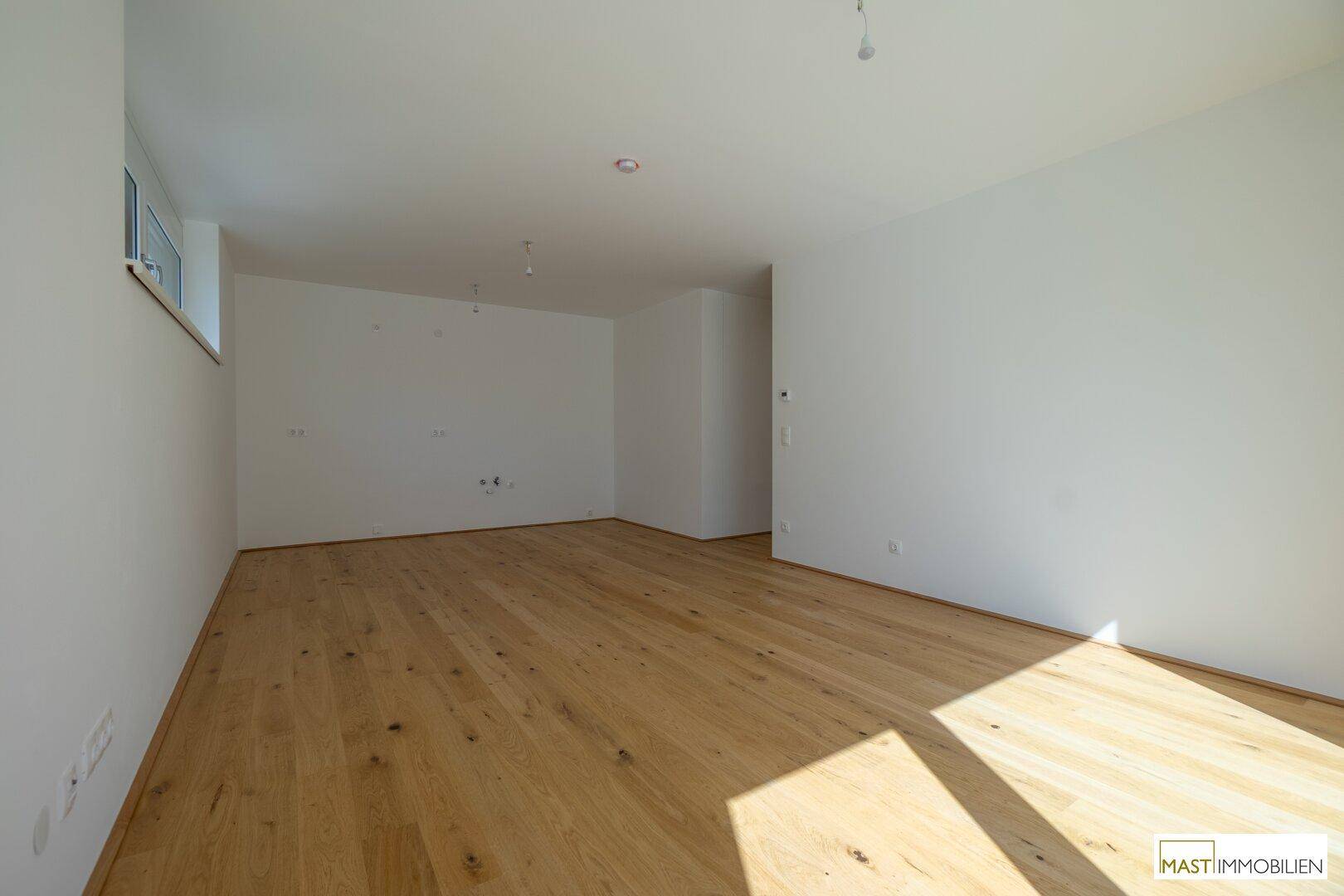 Geräumiger, heller Raum mit Holzboden und viel Tageslicht, ideal als Wohnzimmer.