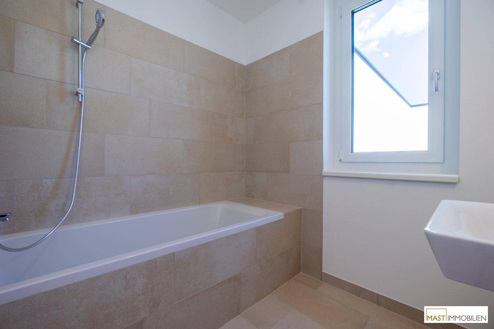 Modernes Badezimmer mit Badewanne, Waschbecken und Fenster für Tageslicht.