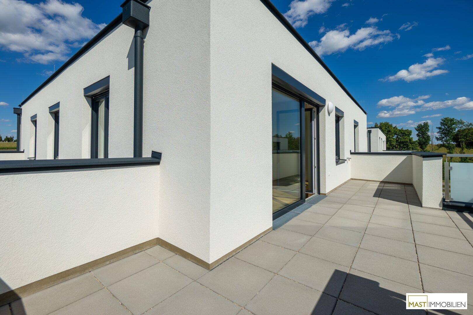Moderne Gebäudefassade mit großer Terrasse und Blick auf die umliegende Neubausiedlung.